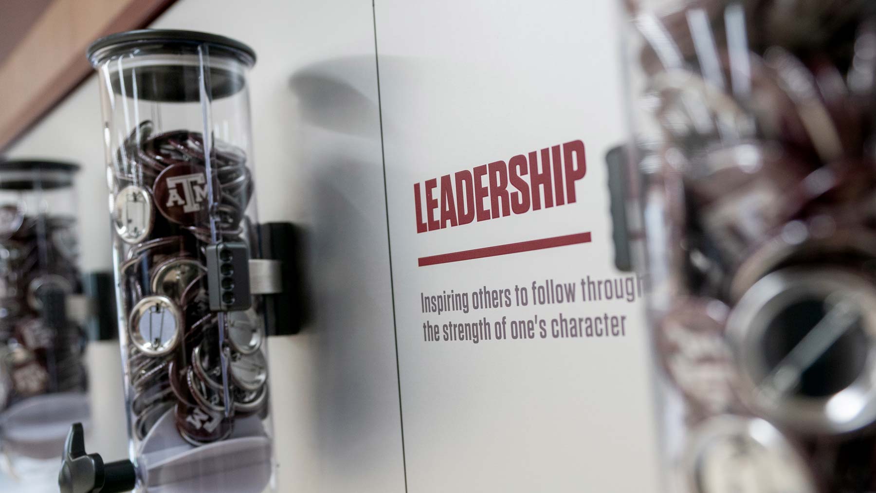 Buttons with the Texas A&M logo on them sit in a plastic container next to a sign that reads: "Leadership: Inspiring others to follow through the strength of one's character"