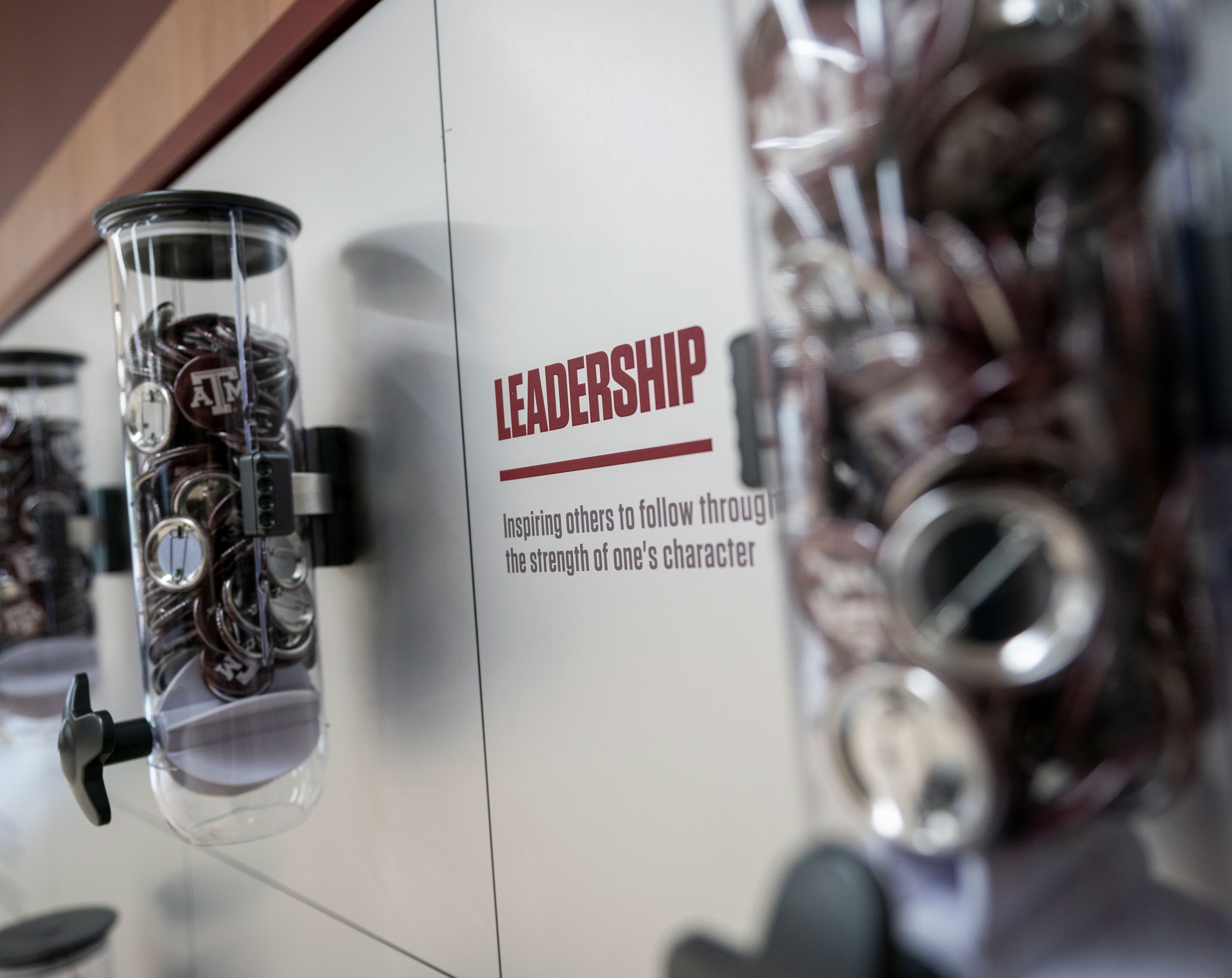 Buttons with the Texas A&M logo on them sit in a plastic container next to a sign that reads: "Leadership: Inspiring others to follow through the strength of one's character"